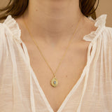 Gold necklace with a pendant worn by a person in a white blouse.