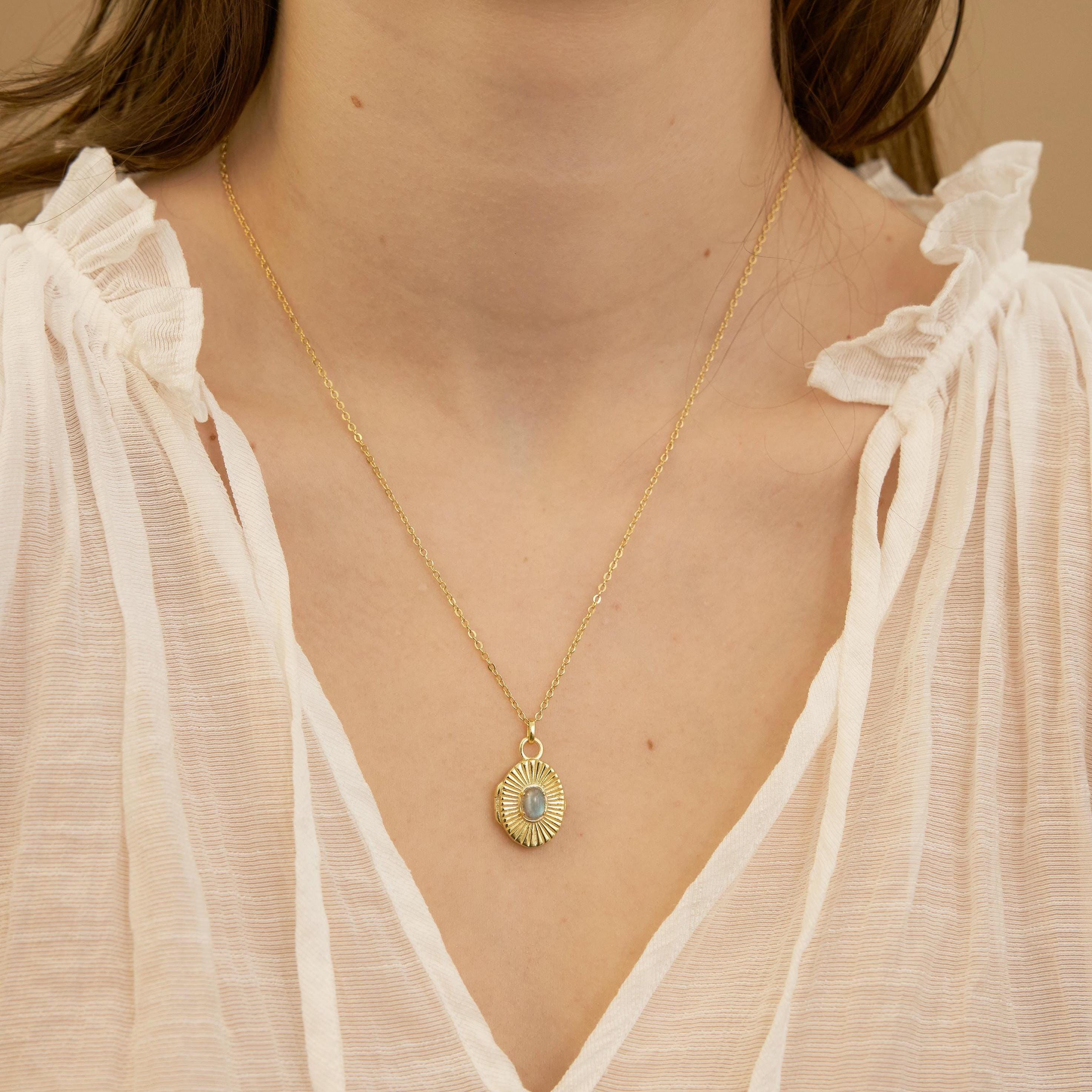 Gold necklace with a pendant worn by a person in a white blouse.