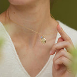 Close-up of a person wearing a gold necklace with a pendant, with a blurred green background.