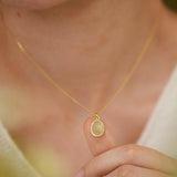 A person wearing a gold necklace is holding up a small, round pendant on their finger.