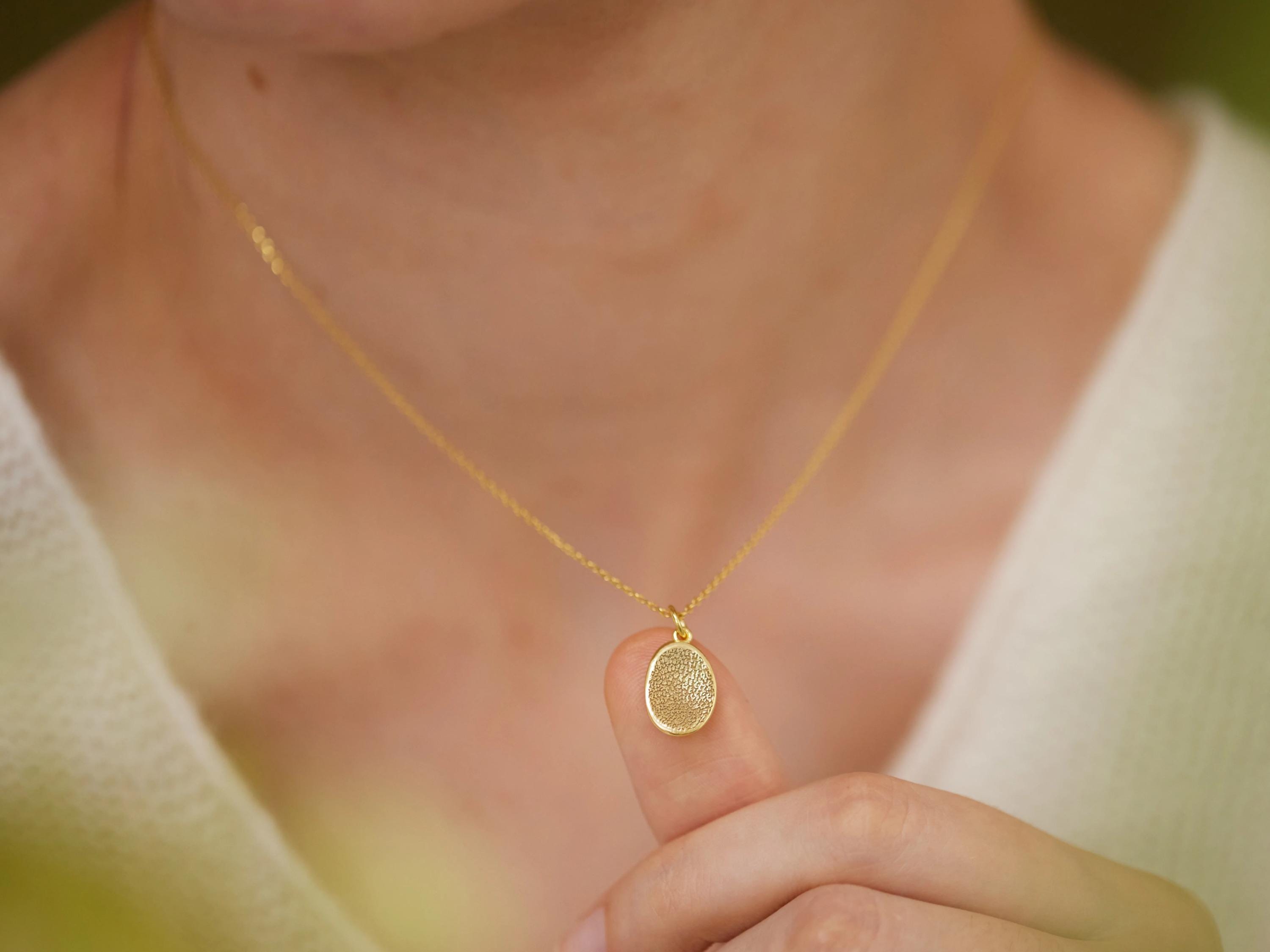 A person wearing a gold necklace is holding up a small, round pendant on their finger.