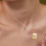 A close-up of a person's neck and chest area wearing a gold necklace with a pendant.