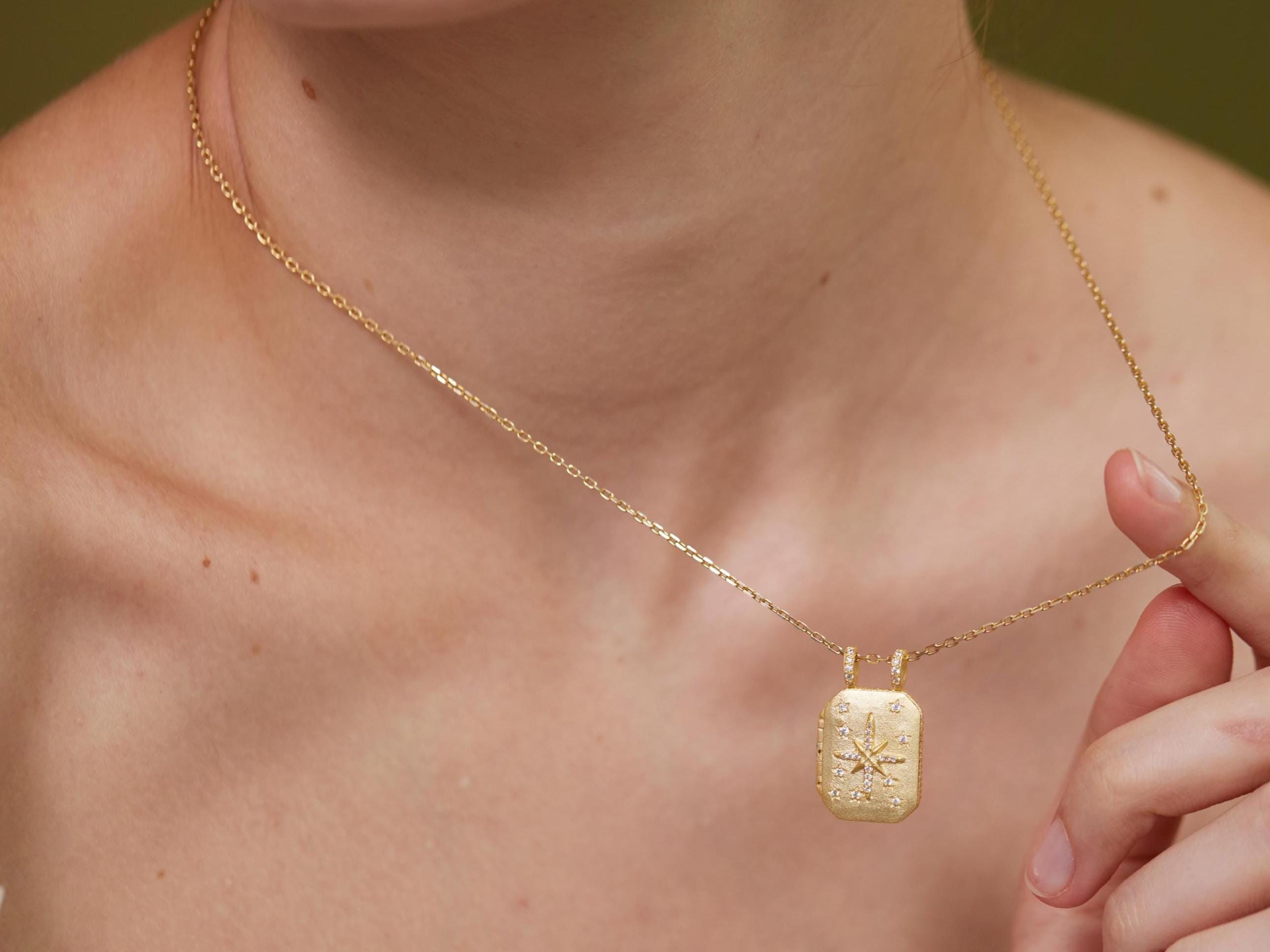 A close-up of a person&#39;s neck and chest area wearing a gold necklace with a pendant.