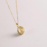 Gold necklace with a sunburst pendant on a light gray background