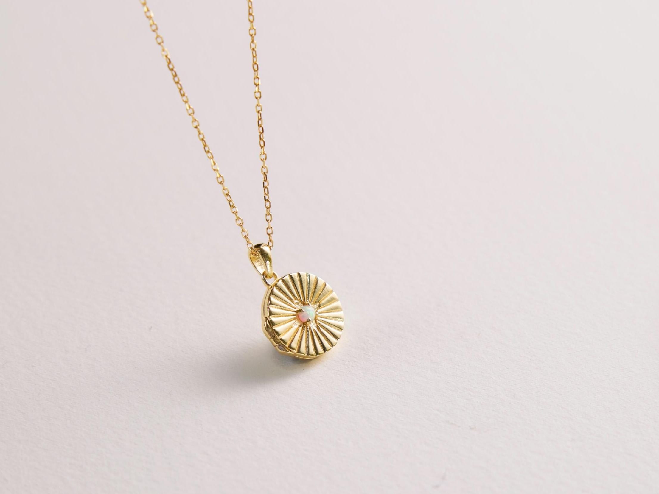 Gold necklace with a sunburst pendant on a light gray background