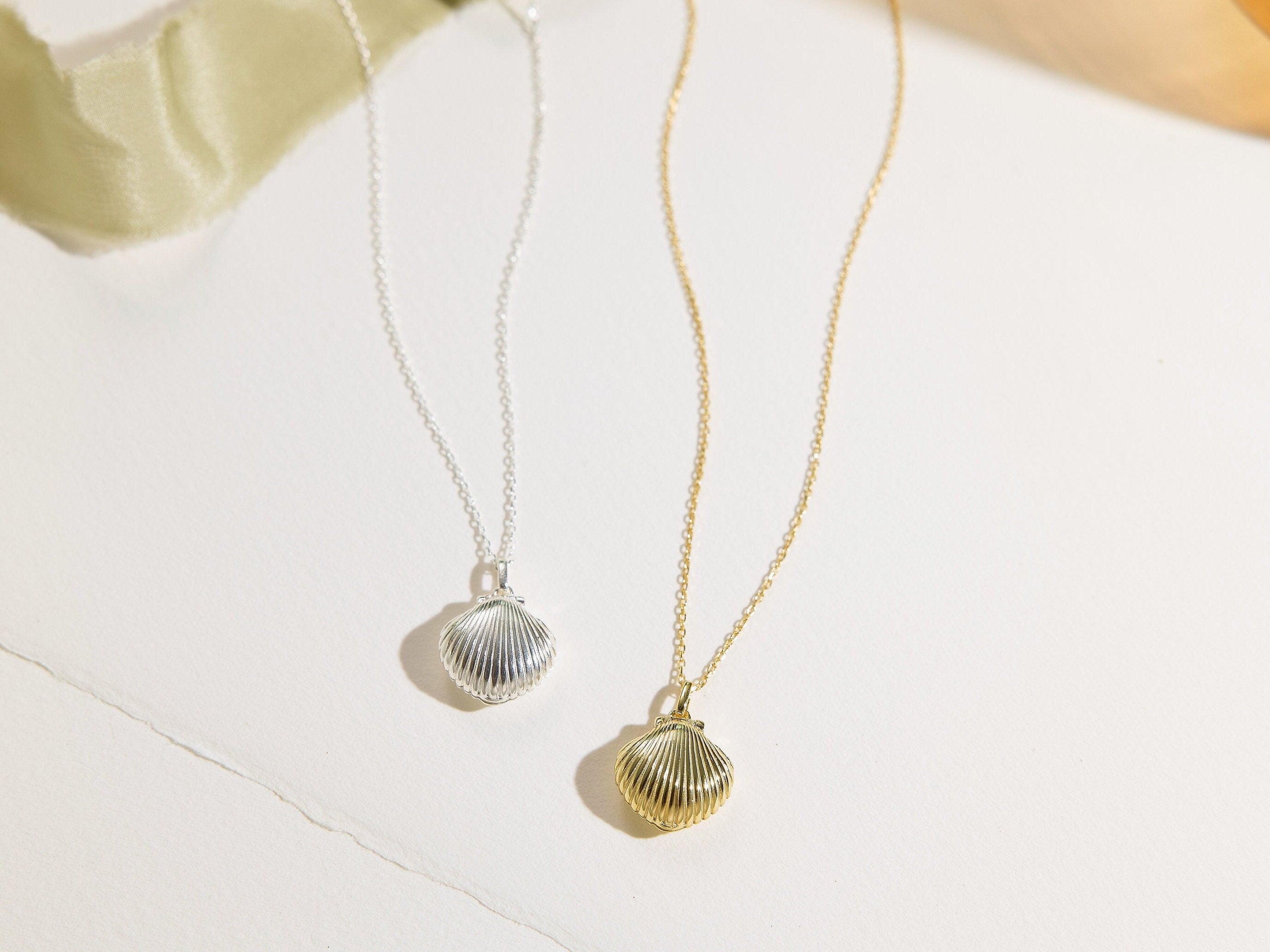 Two shell-shaped pendant necklaces on a light background