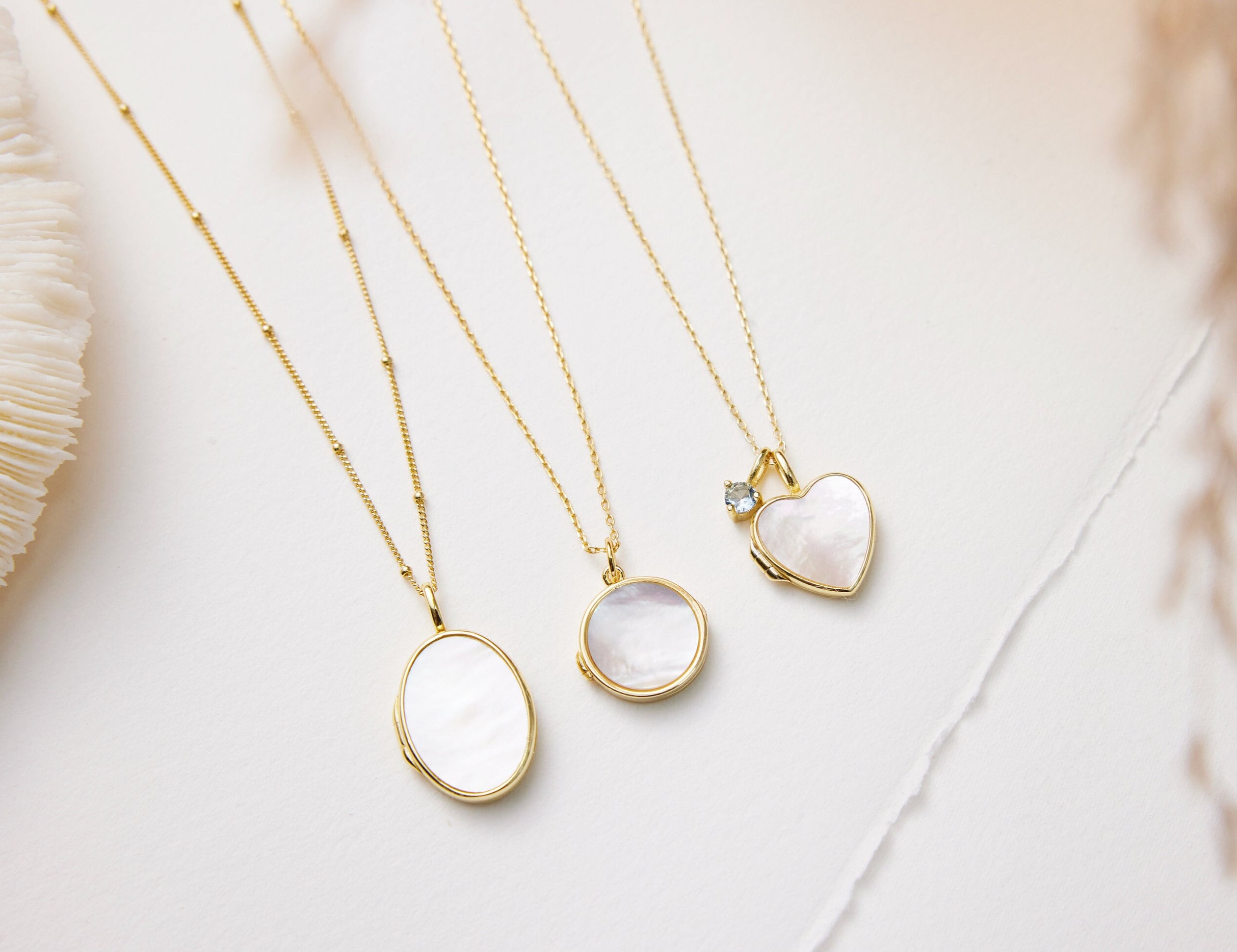 Three gold necklaces with different pendants on a light background