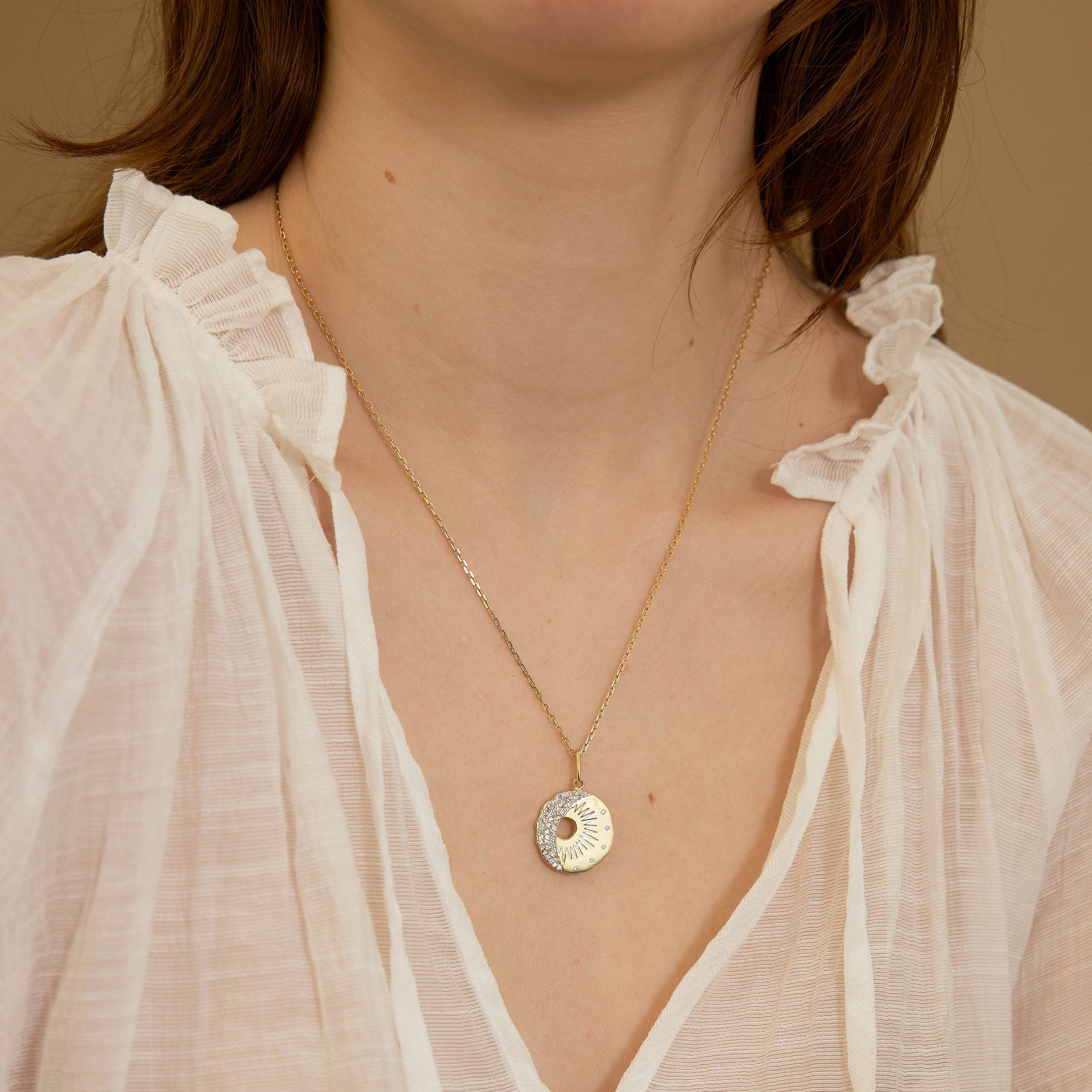 Gold necklace with a circular pendant worn by a person in a light blouse against a neutral background