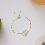 Gold bracelet with a circular design on a white surface next to a green fruit.