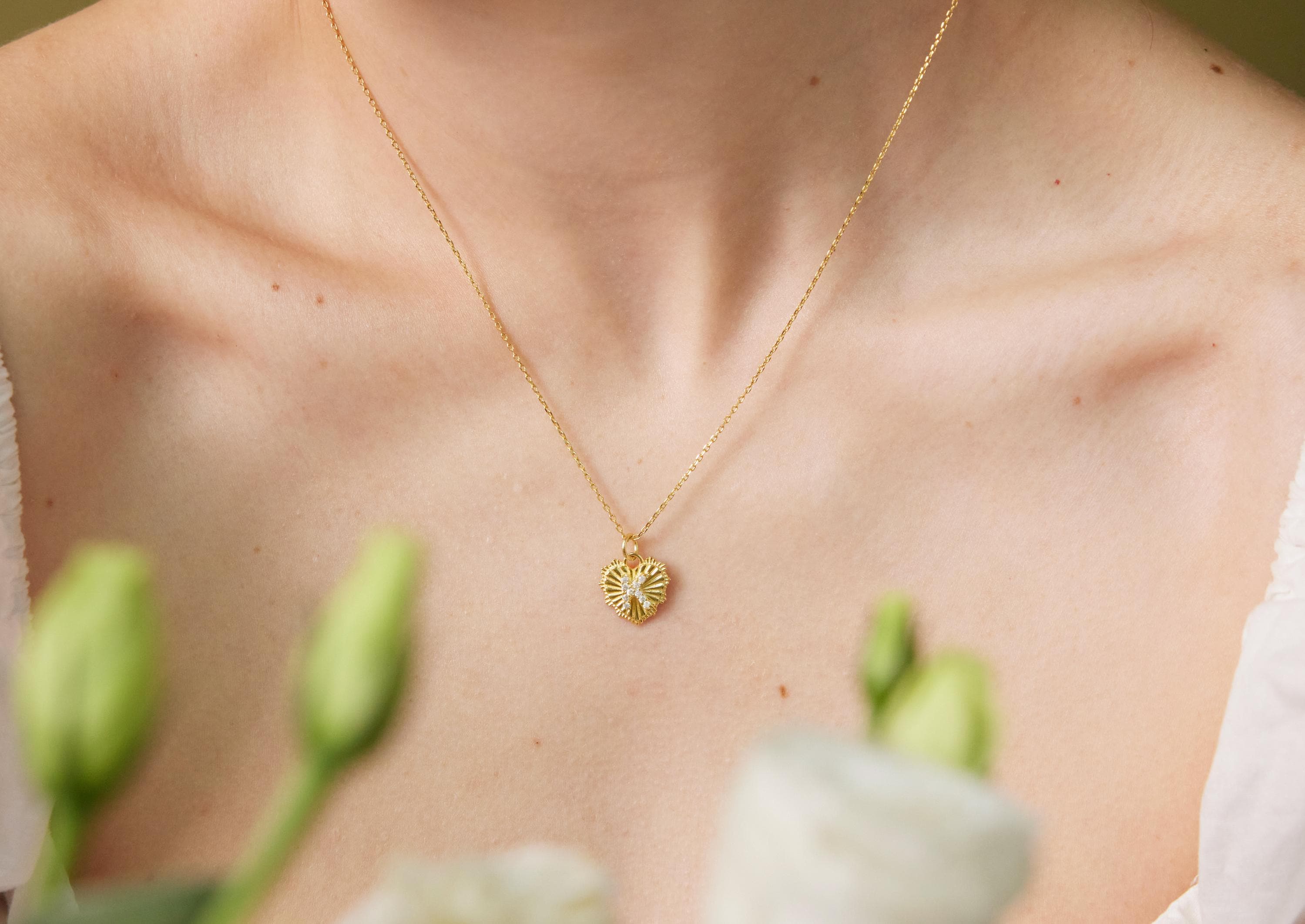 Gold necklace with a floral pendant on a person's neck, with green flowers in the background.