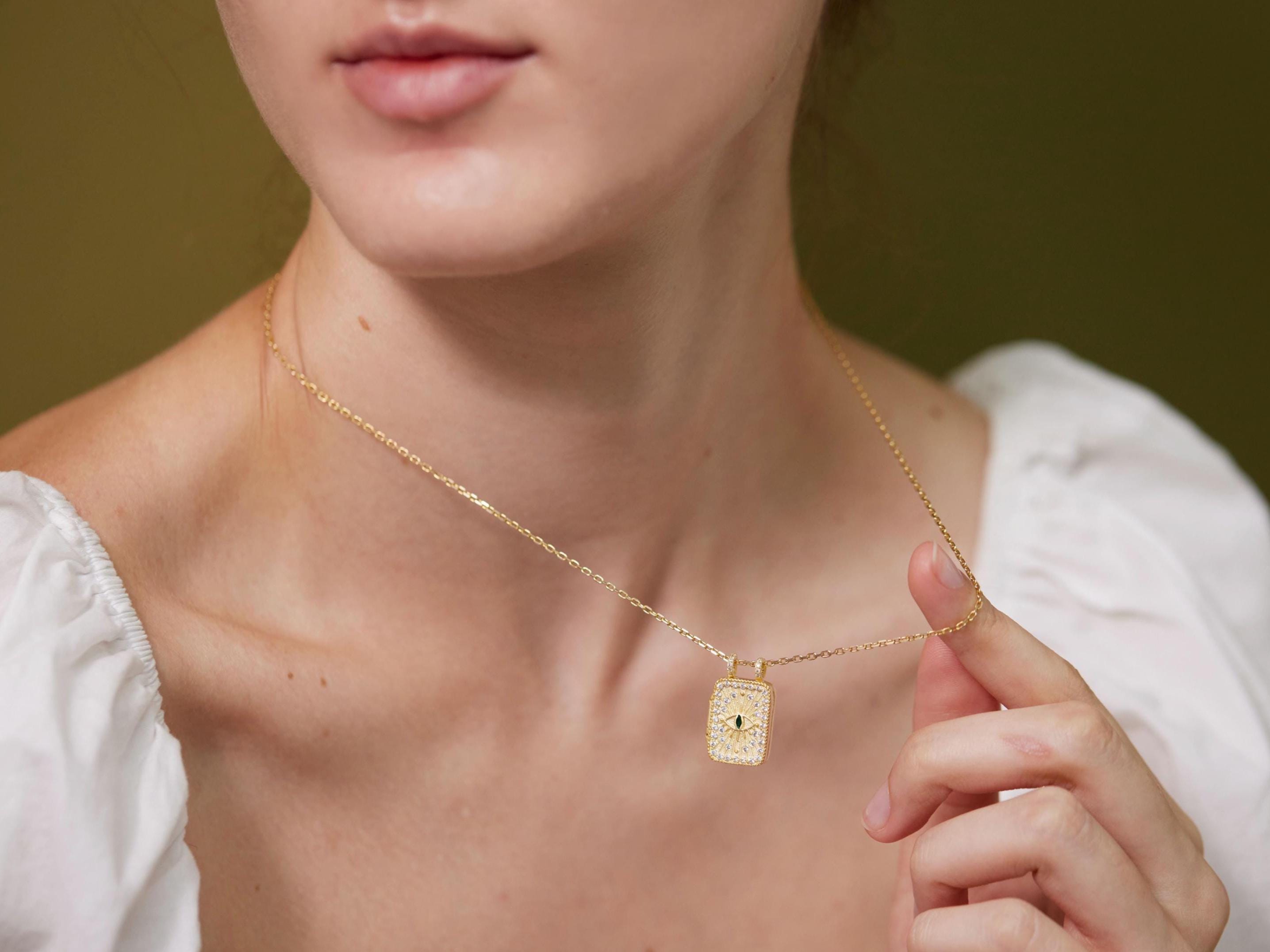 A close-up of a woman wearing a gold necklace with a pendant, posing against a green background.