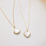 Two gold necklaces with heart and round pendants on a light background