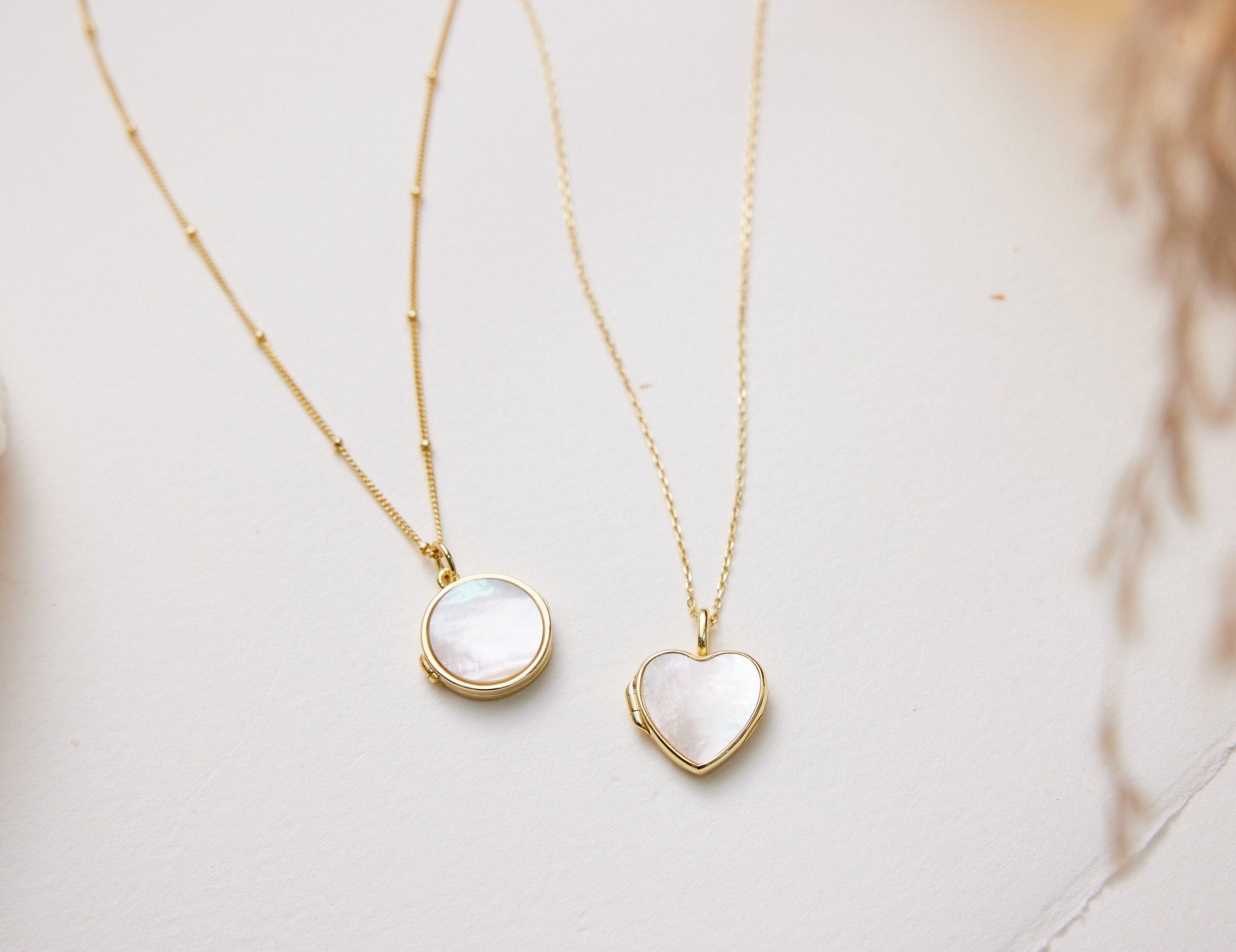 Two gold necklaces with heart and round pendants on a light background