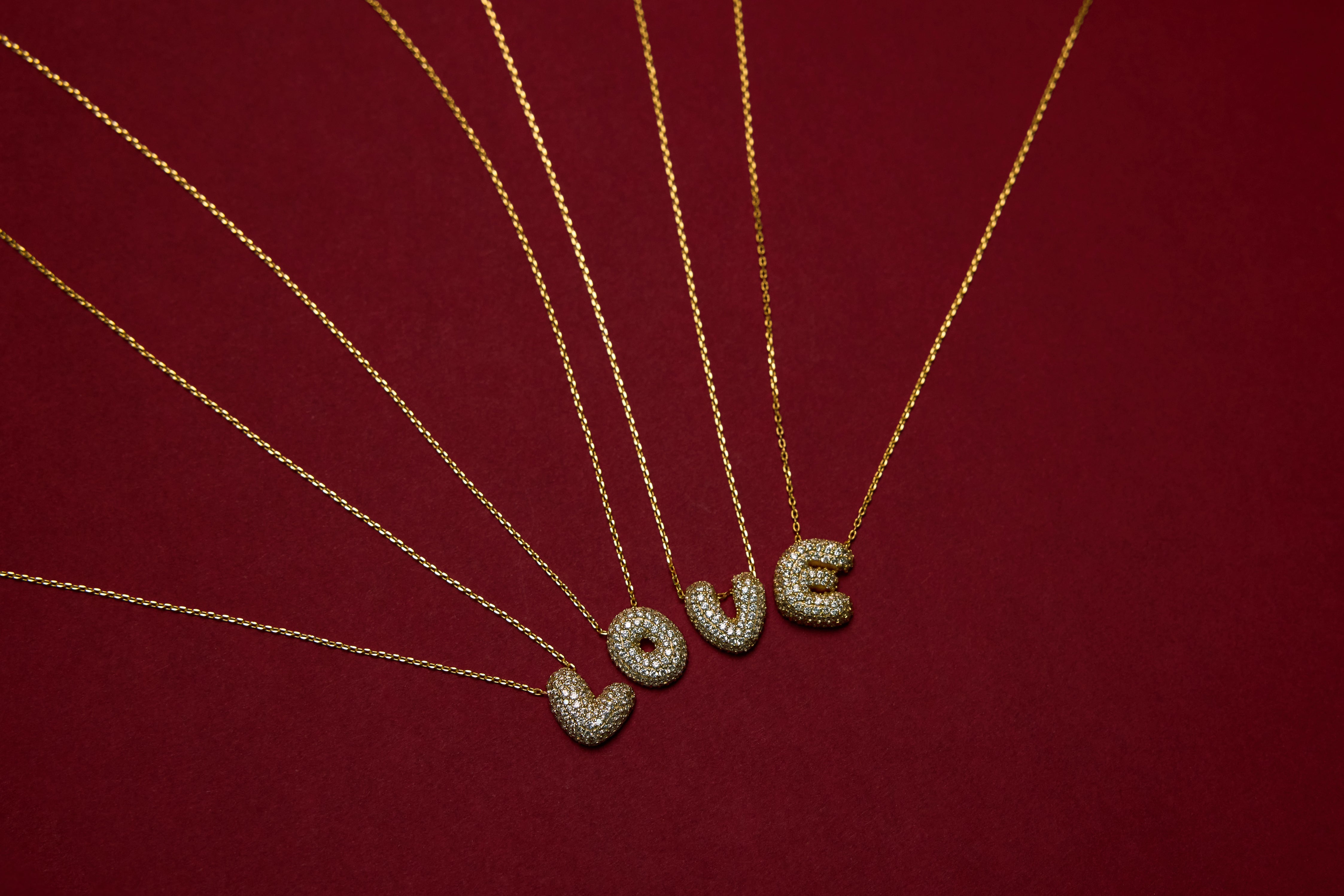 Gold necklaces with 'LOVE' pendants on a red background