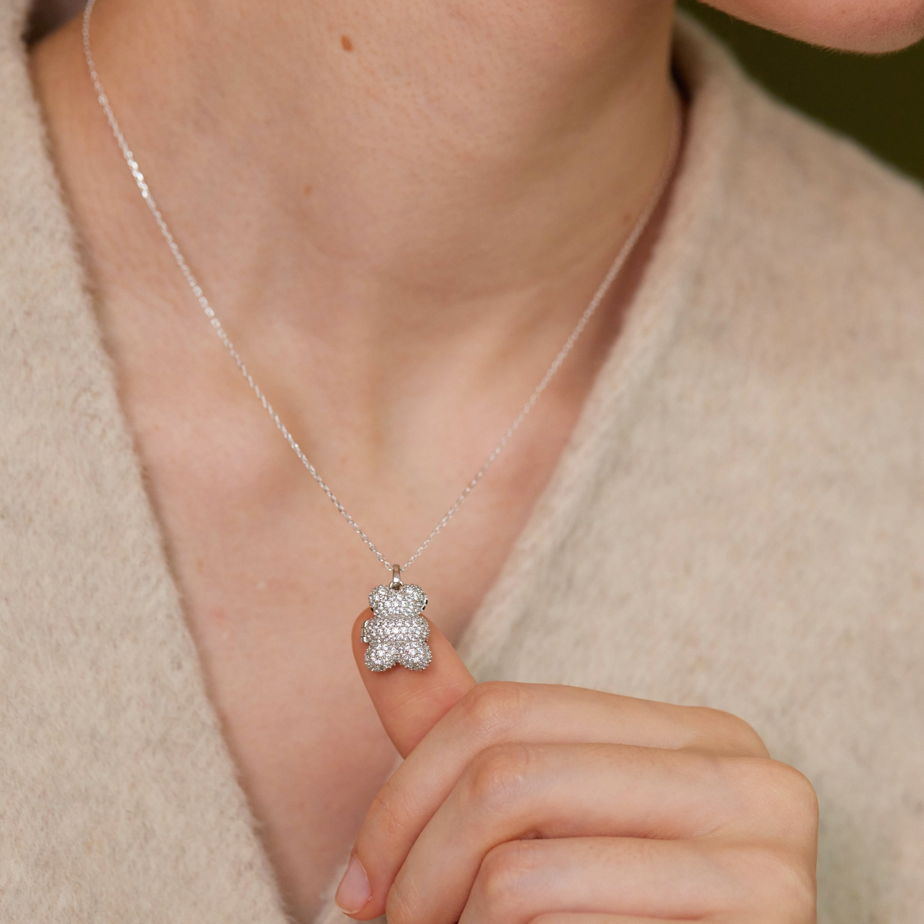 Silver necklace with a teddy bear pendant worn by a person.
