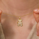 Gold necklace with a bear-shaped pendant held by hands against a neutral background