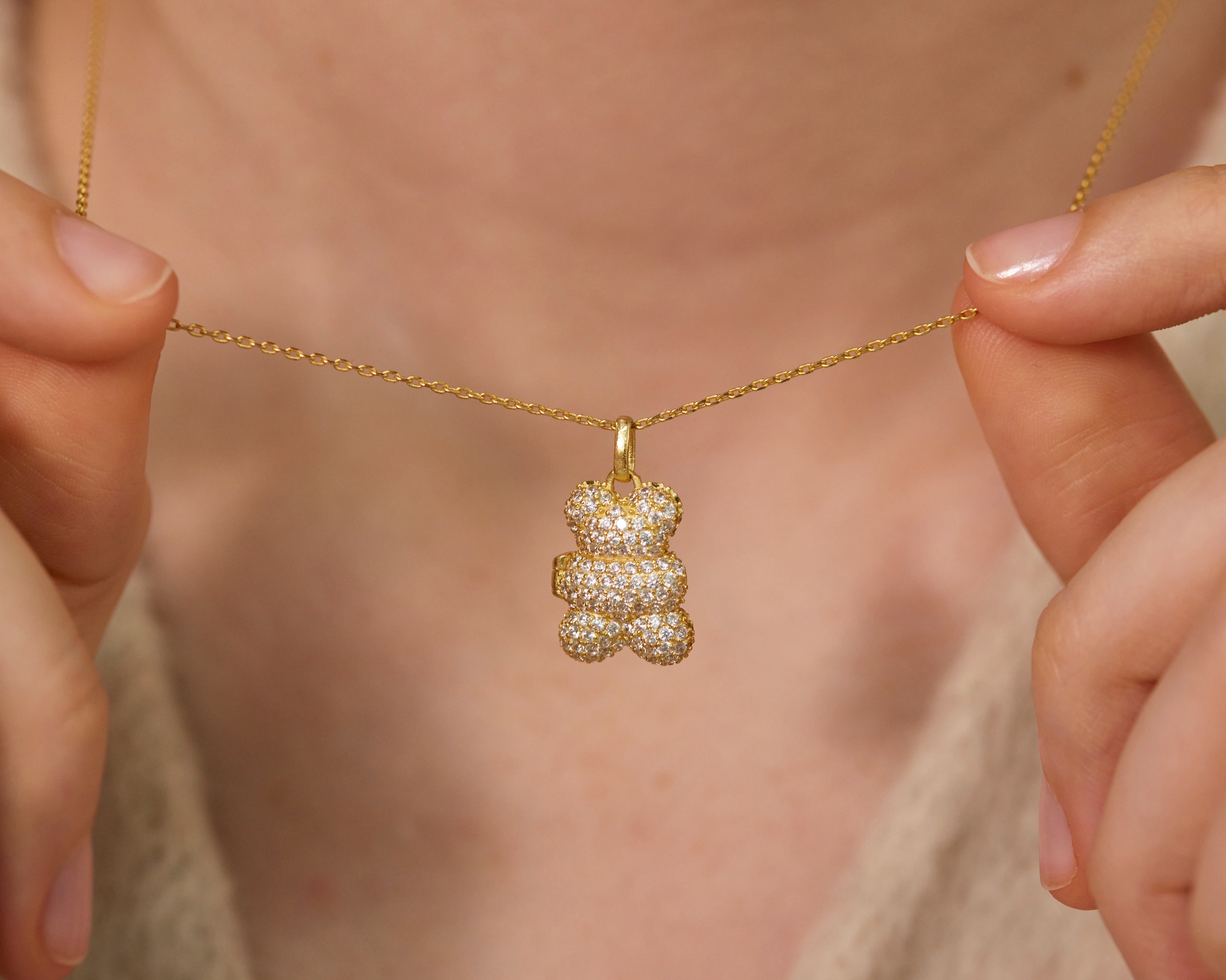 Gold necklace with a bear-shaped pendant held by hands against a neutral background