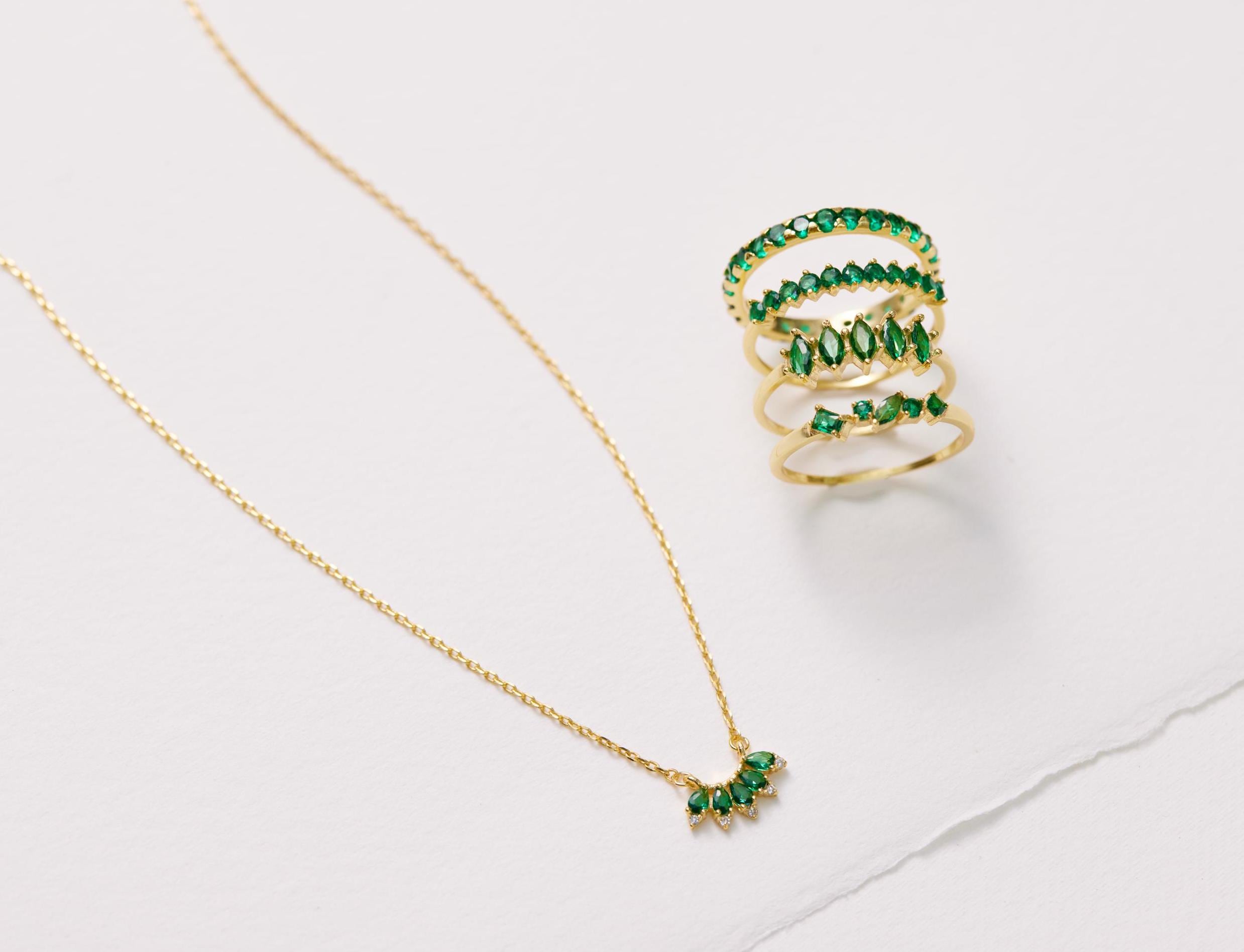 Gold necklace and ring with green gemstones on a white background