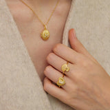 A close-up of a person's hand wearing three gold-colored rings with unique designs, including a ring with a shell-like pattern and another ring with a heart-shaped design.