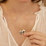 Gold necklace with a pendant featuring two small images, worn by a person in a light-colored top.