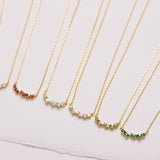 Set of gold necklaces with small gemstones on a light pink background