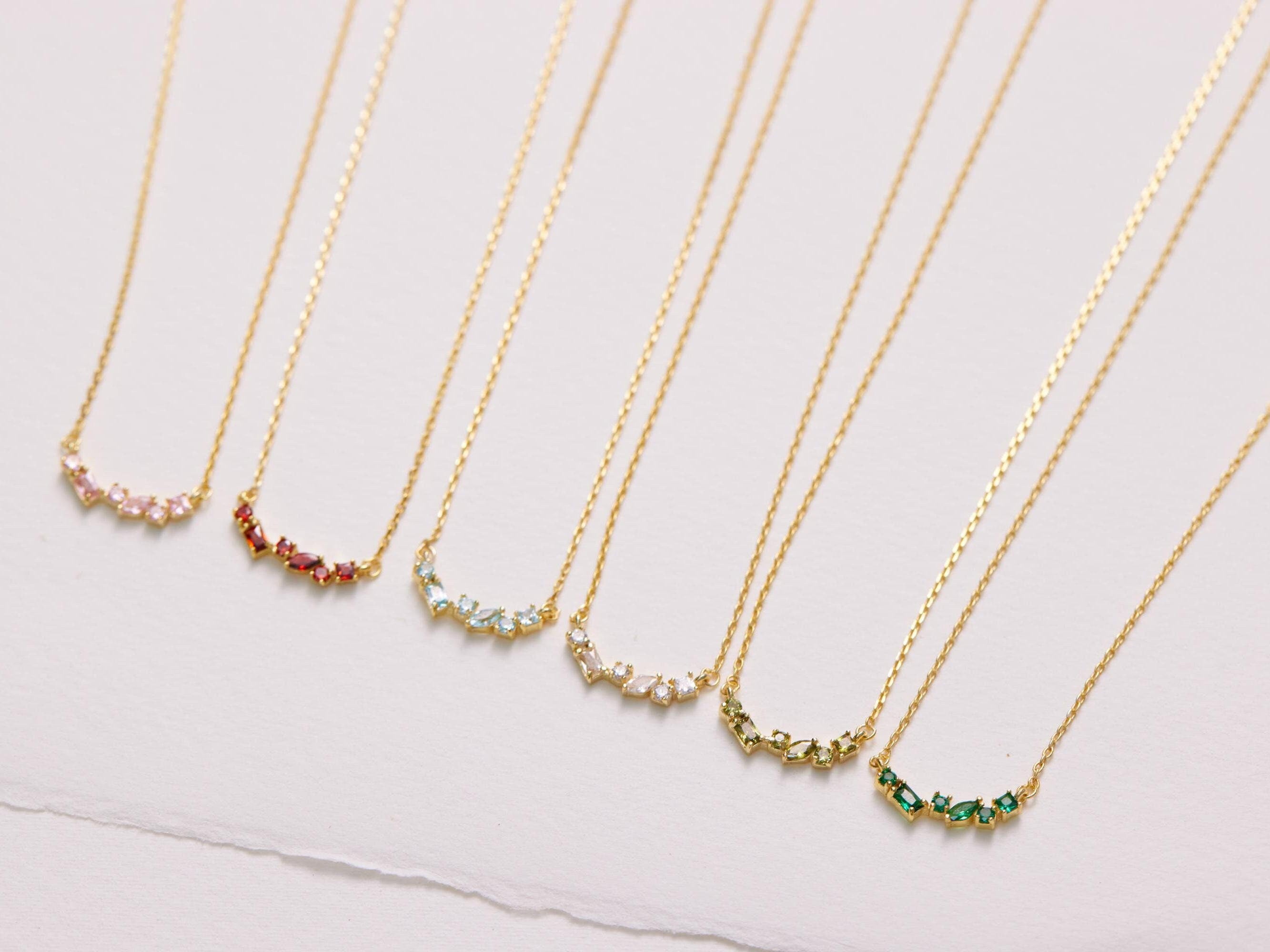 Set of gold necklaces with small gemstones on a light pink background