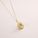 Gold necklace with a round pendant on a light pink background