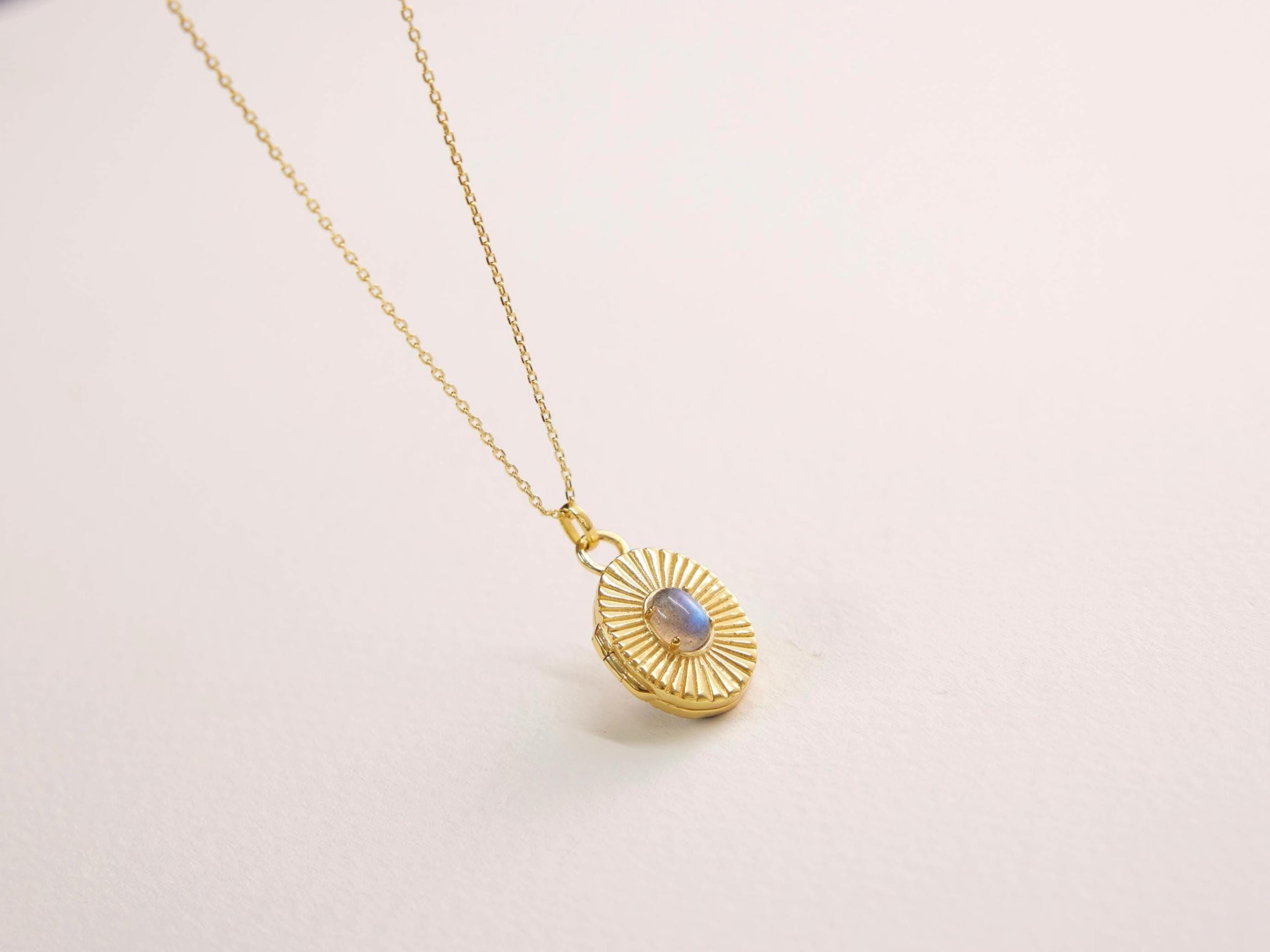 Gold necklace with a round pendant on a light pink background