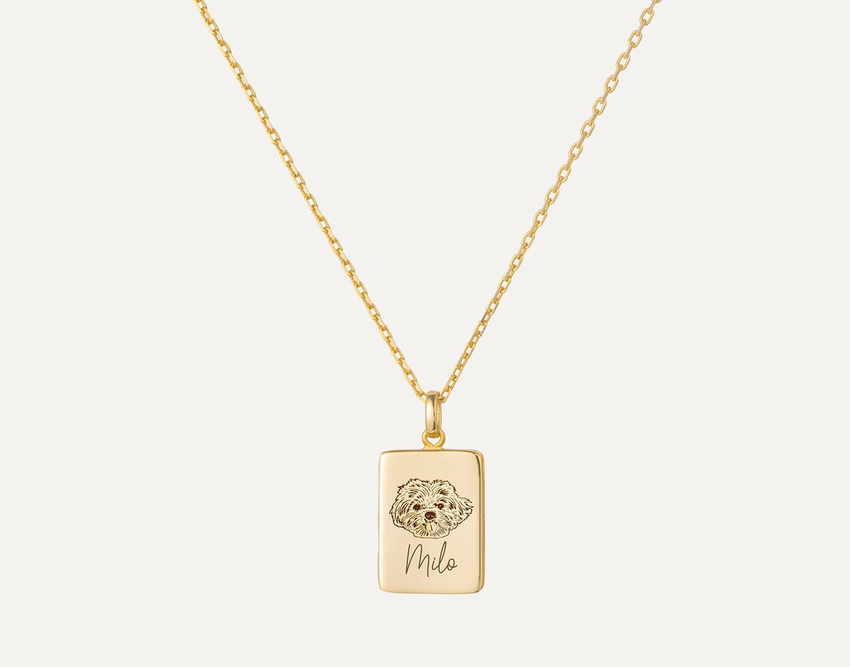 Gold necklace with a pendant featuring a dog illustration and engraved text on a white background