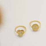 Two gold heart-shaped rings with the letters "E" and "A" on them, placed on a white background.