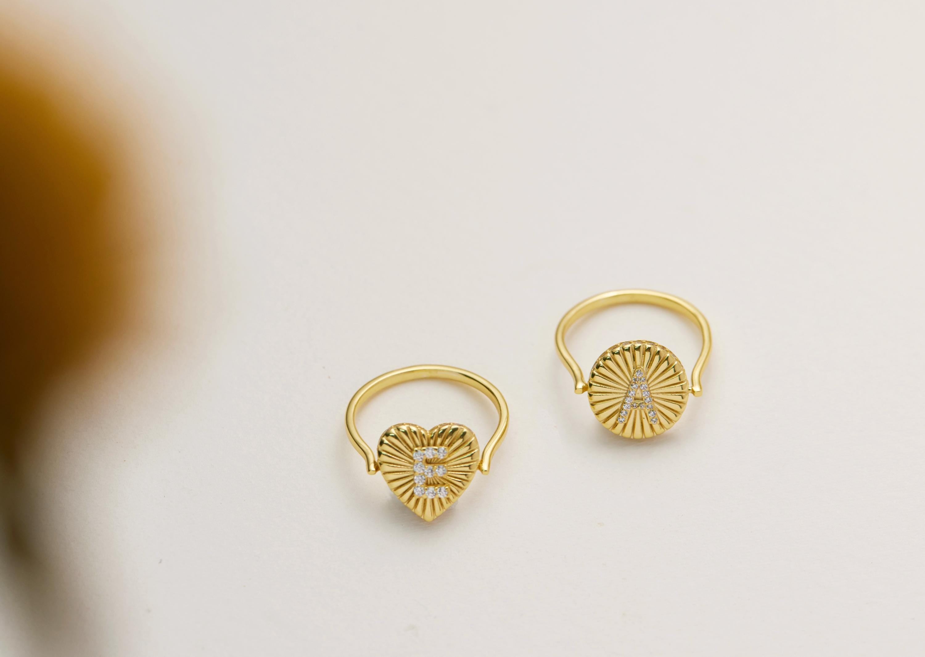 Two gold heart-shaped rings with the letters "E" and "A" on them, placed on a white background.
