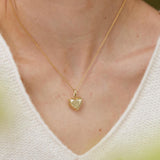 A gold heart-shaped pendant necklace is worn by a person in a white sweater.