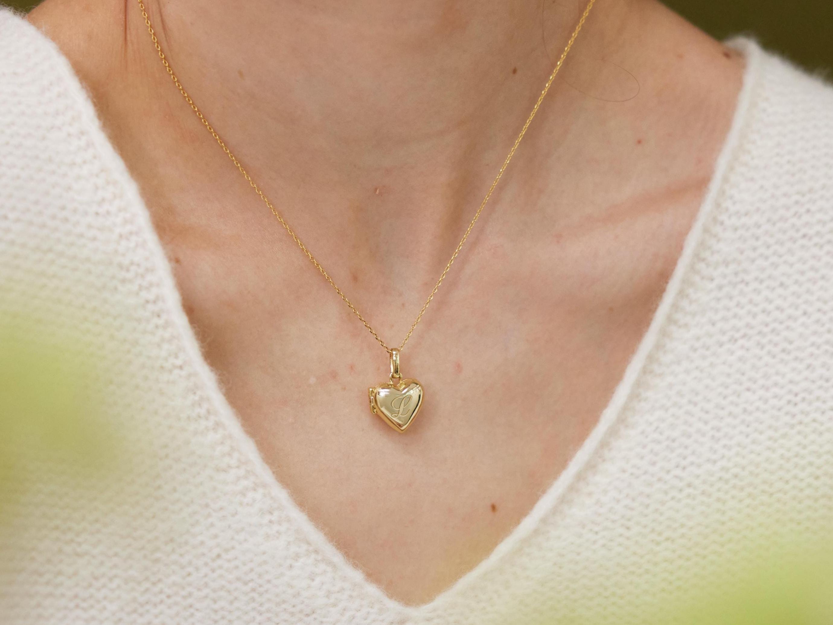 A gold heart-shaped pendant necklace is worn by a person in a white sweater.