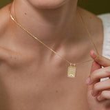 A close-up of a person's neck and chest wearing a gold necklace with a pendant.