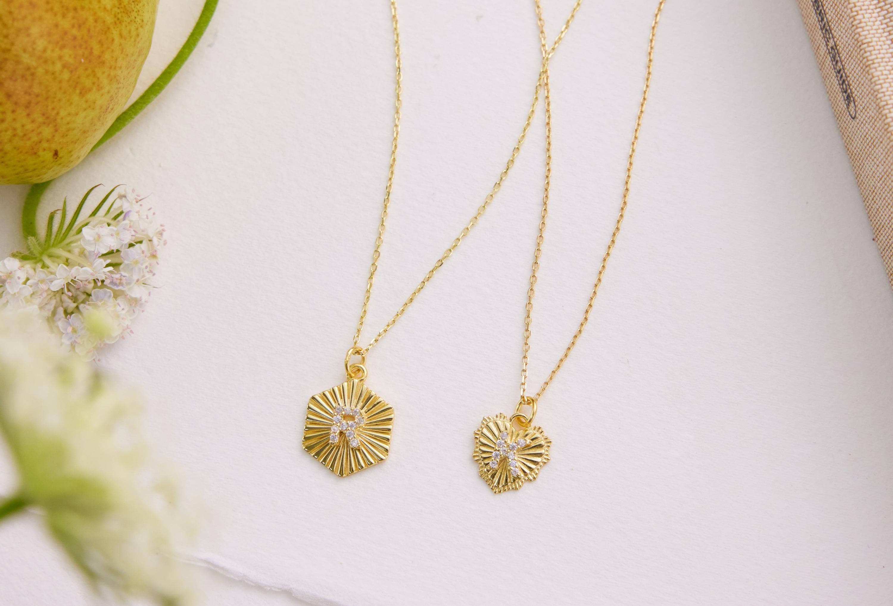 Two gold necklaces with circular pendants on a white surface with flowers and an apple.