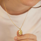 Gold necklace with a paw print pendant held by a person against a neutral background