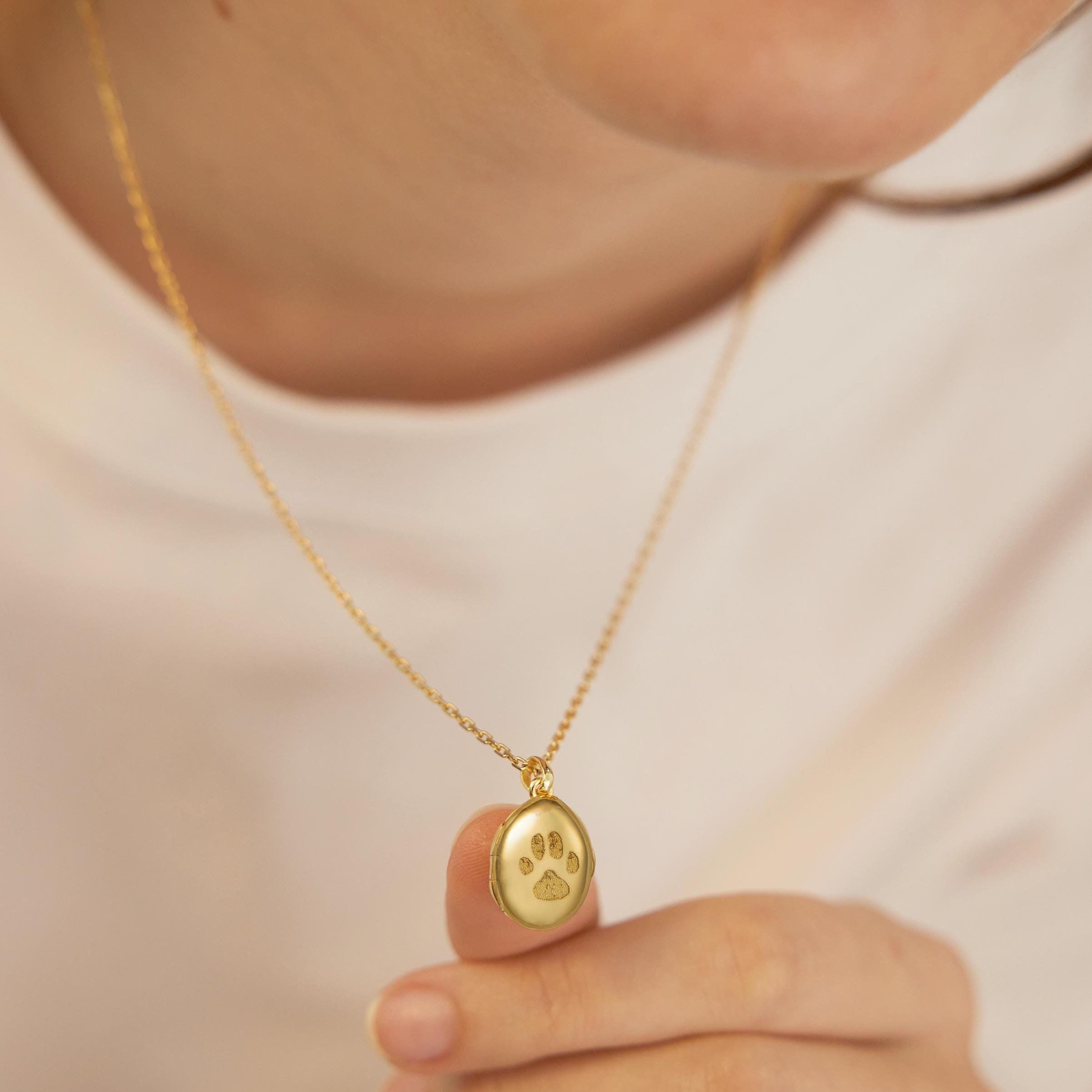 Gold necklace with a paw print pendant held by a person against a neutral background