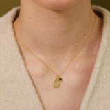 A gold necklace with a small oval-shaped pendant is worn around a person's neck.