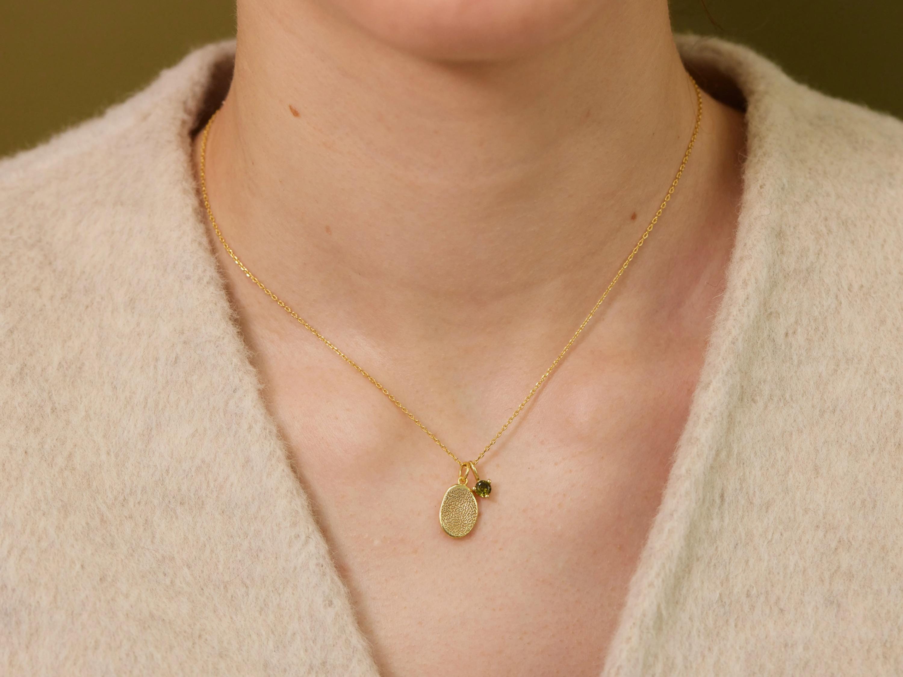 A gold necklace with a small oval-shaped pendant is worn around a person's neck.