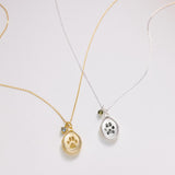 Two gold and silver paw print necklaces on a light gray background