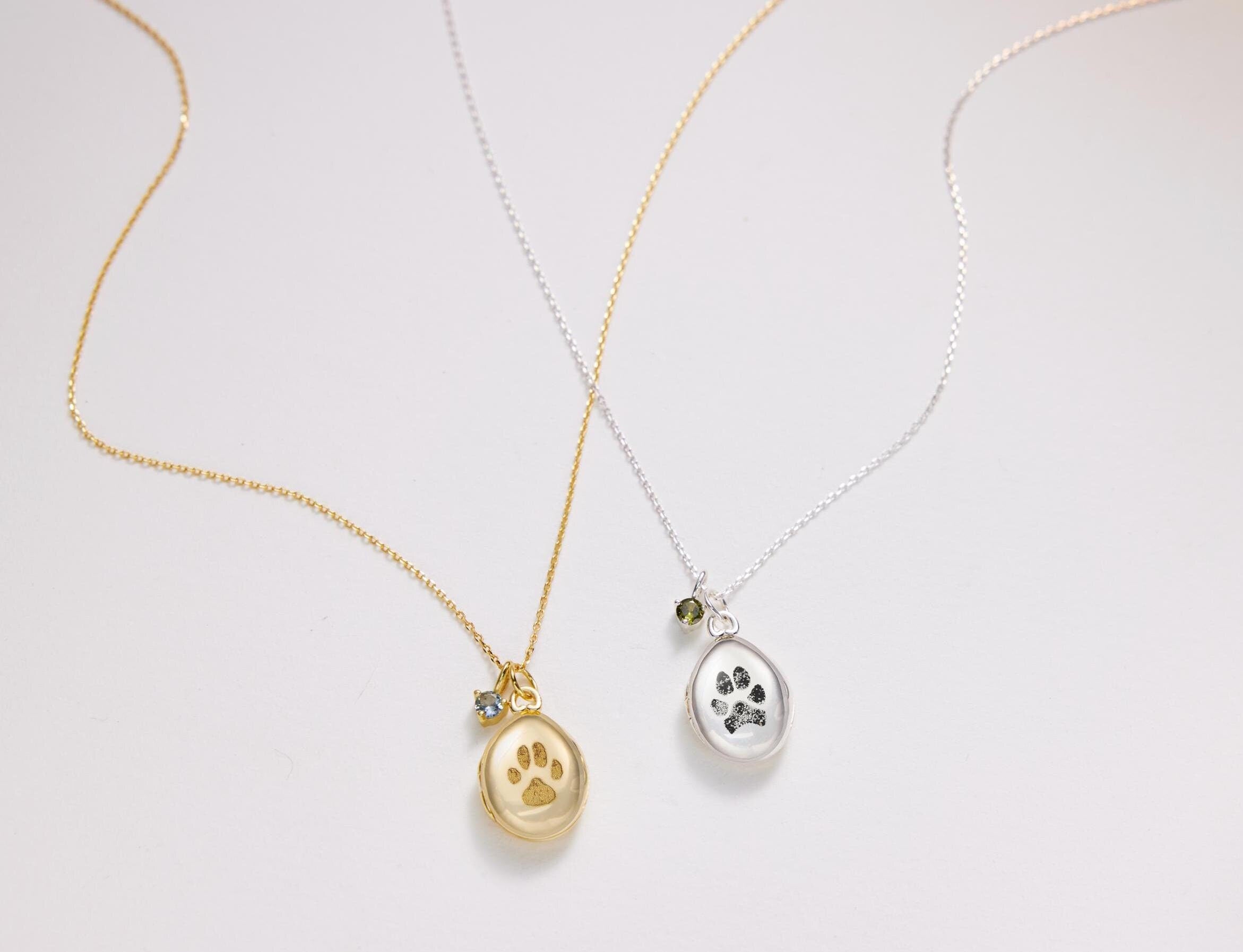 Two gold and silver paw print necklaces on a light gray background