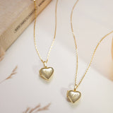 Two gold heart-shaped locket necklaces on a marble surface.