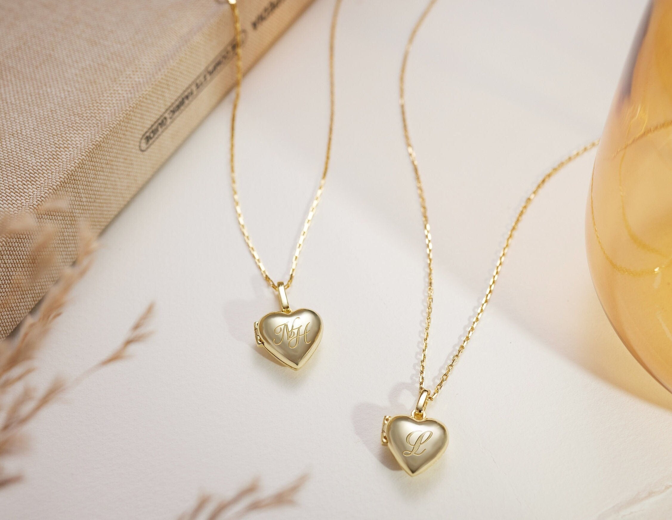 Two gold heart-shaped locket necklaces on a marble surface.