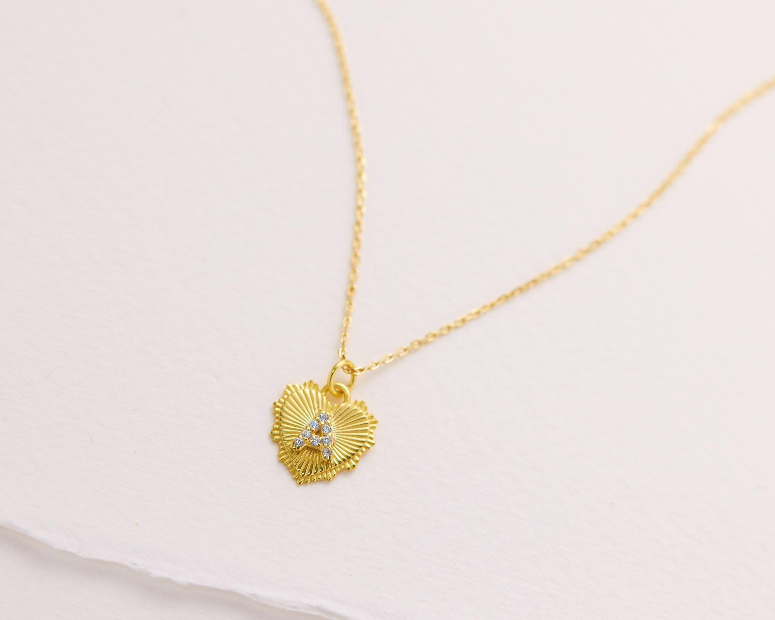 A delicate gold heart-shaped pendant necklace with a small gemstone is displayed against a plain white background.
