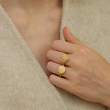 A close-up of a person's hand wearing two gold rings with unique designs.