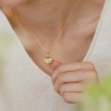 A person wearing a white sweater is holding a small gold heart-shaped charm on their finger.