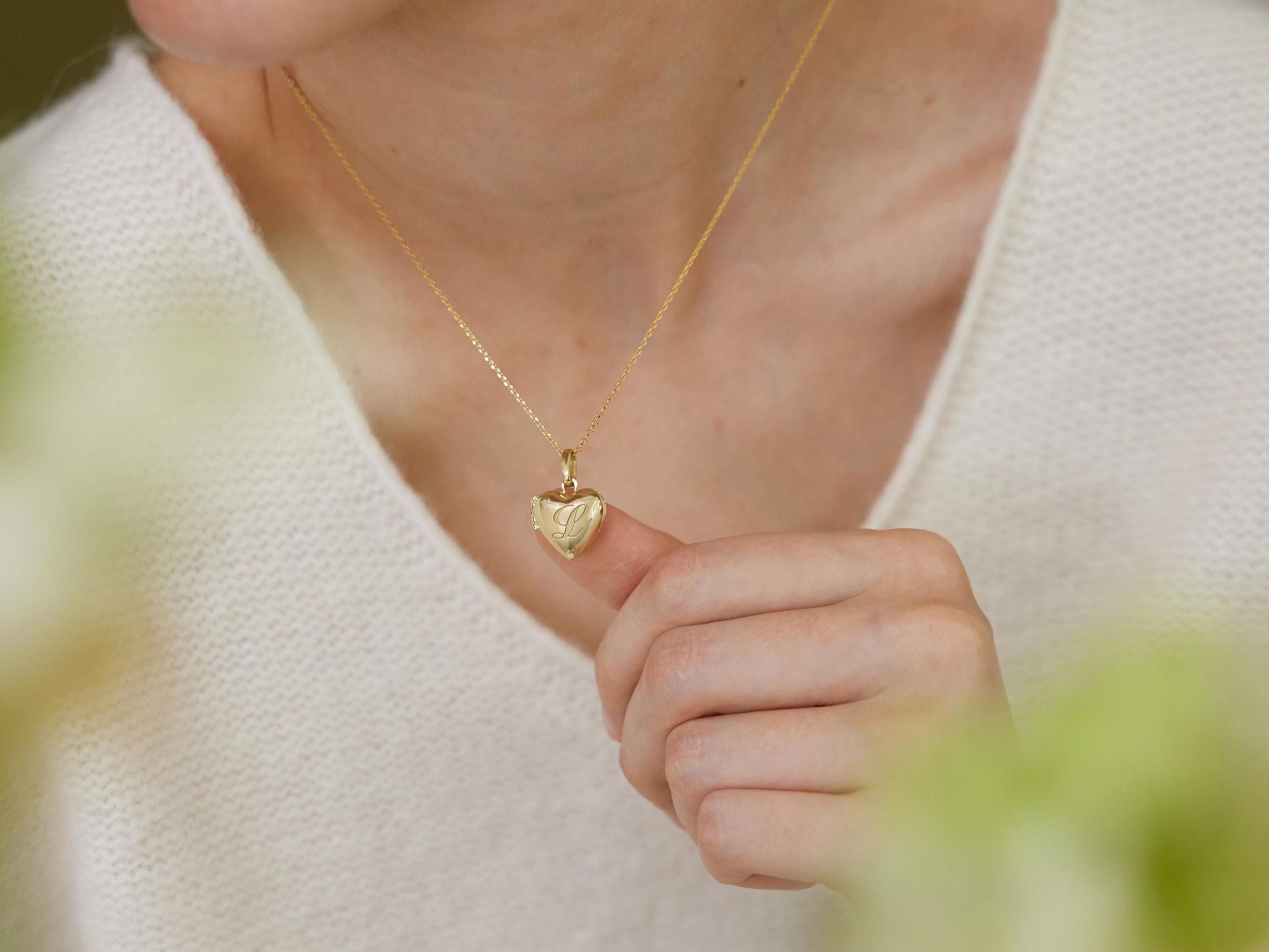 A person wearing a white sweater is holding a small gold heart-shaped charm on their finger.