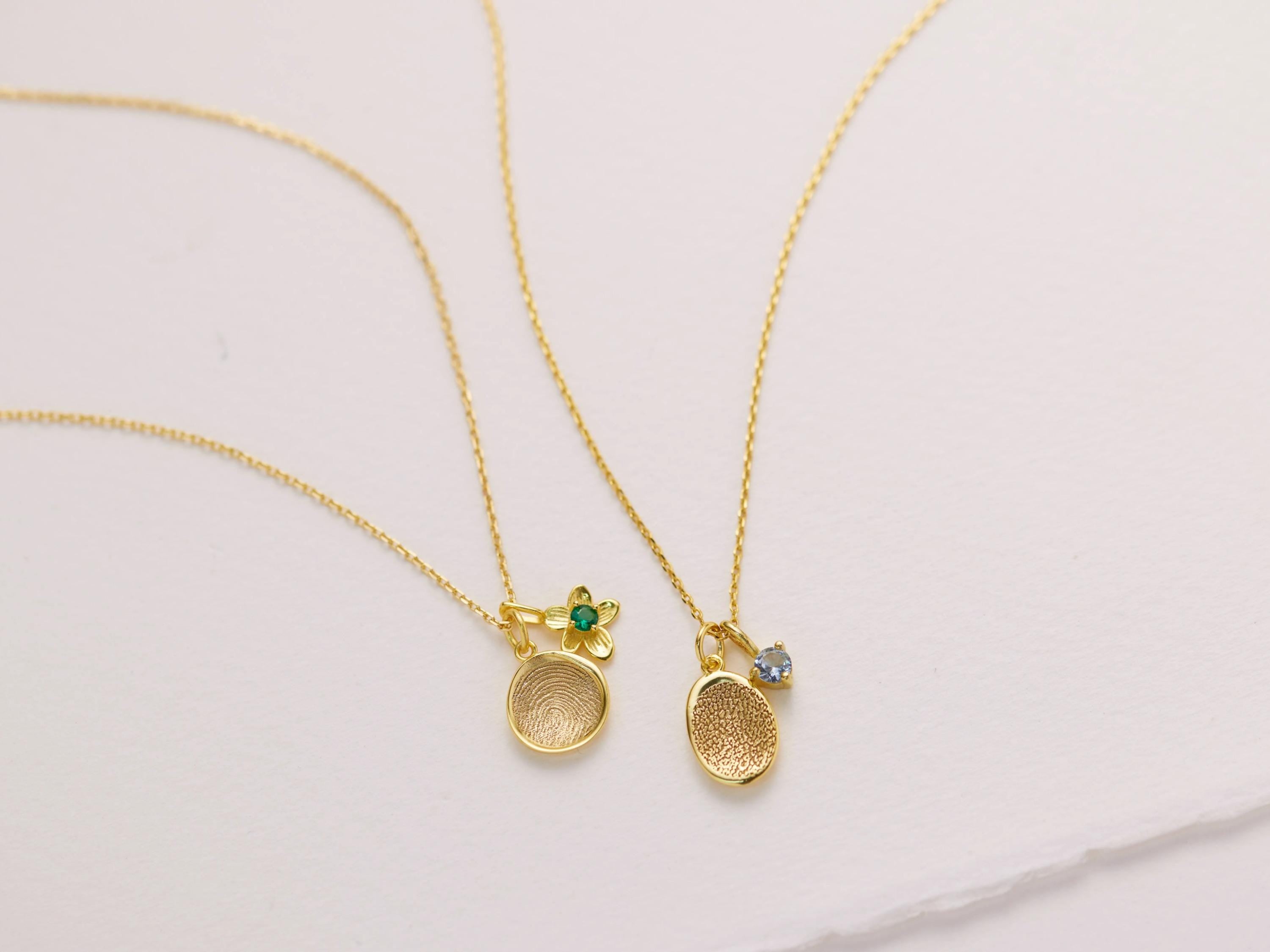Two gold necklaces with pendants are displayed on a white surface.