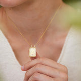 A person wearing a gold necklace with a pendant is holding the pendant up to their face.