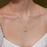 Gold necklace with a pendant on a person wearing a white blouse against a neutral background